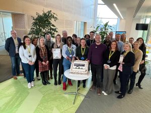 A group of colleagues standing around a cake which has a sustainability logo on it.
