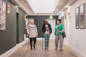 Three women walking down corridor in a residential building chatting to each other